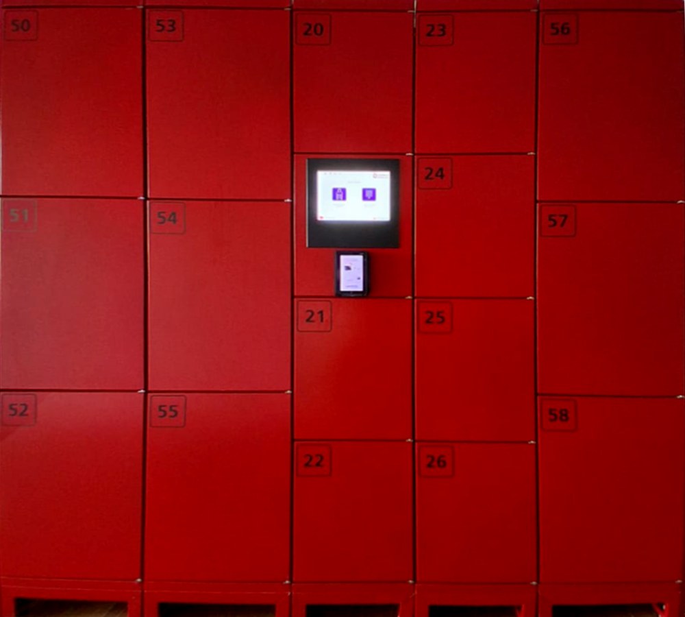 The locker bank at the shop: sixteen numbered red doors in five columns, with the lit payment screen and card reader set into the middle column